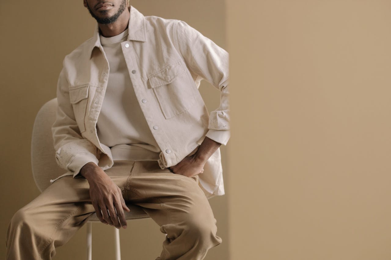 Minimalistic portrait of a man wearing a beige jacket and pants, sitting casually indoors with neutral tones.